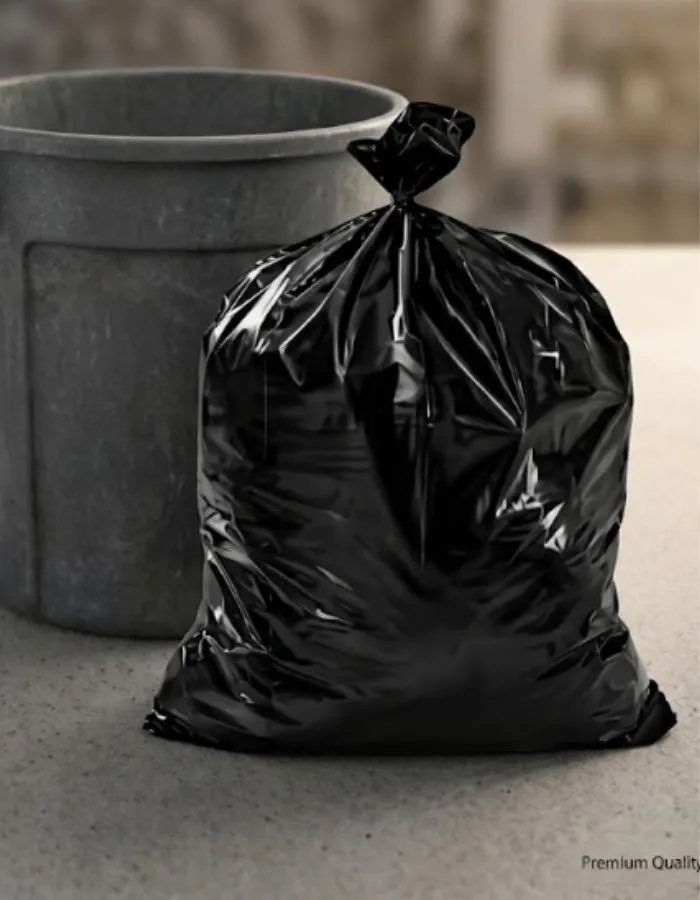 A filled black polythene garbage bag tied at the top beside a bin